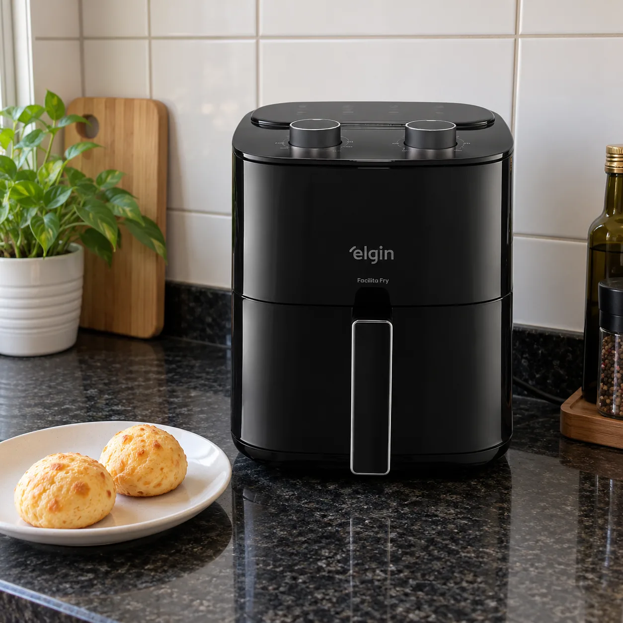 Air fryer Elgin pequena e preta, de dois botões giratórios, na bancada de uma cozinha de azulejo branco, ao lado de um prato com pães de queijo